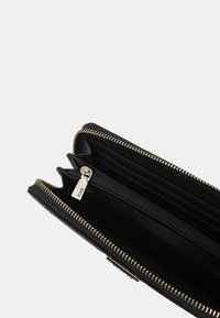 Portafoglio in pelle nera con zip in tono dorato, dotato di più scomparti, una tasca con zip e una superficie liscia. Logo visibile sulla zip.