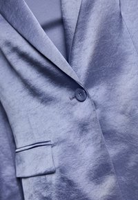 Single-buttoned purple velvet blazer with notch lapel and flap pocket, showing fabric texture and sheen.