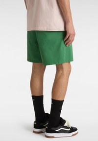 Grønne bomuldsshorts med lige snit, opstribede kanter, bæres med sorte sokker og sneakers med hvide snørebånd og gummisåler.
