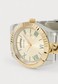 Silver and gold stainless steel watch with a cream face, green Roman numerals, and date display. Features a textured gold bezel and crown.