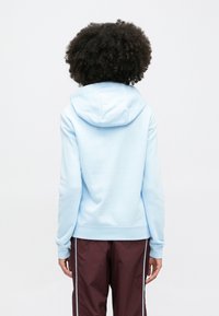 Svetlomodrá mikina s kapucňou na šnúrku, rebrovanými manžetami a lemom. Nosená s tmavomodrými nohavicami s ľahkými svetlomodrými bočnými pruhmi.