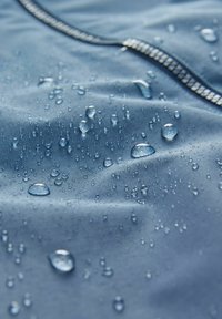 Tessuto blu idrorepellente con gocce visibili. Texture liscia con una leggera lucentezza e motivi geometrici lungo la cucitura.