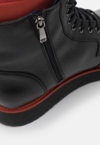 Černá kožená bota s bočním zipem, šněrováním vpředu, červenou podšívkou a kontrastní gumovou podrážkou s úzkým červeným akcentem.
