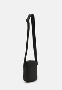 Černá obdélníková crossbody taška vyrobená z hladkého materiálu, s dlouhým nastavitelným popruhem, minimalistickým designem a bez viditelného kování.