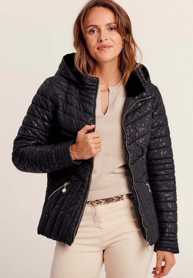 Veste noire matelassée avec capuche, présentant des coutures diagonales et des poches zippées ; tissu doux avec une légère brillance et un col en peluche.