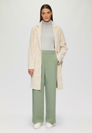 Übergroßer creme- und beige-karierter Mantel, grauer Rollkragenpullover und weite, salbeigrüne Hose, kombiniert mit weißen Sneakern.