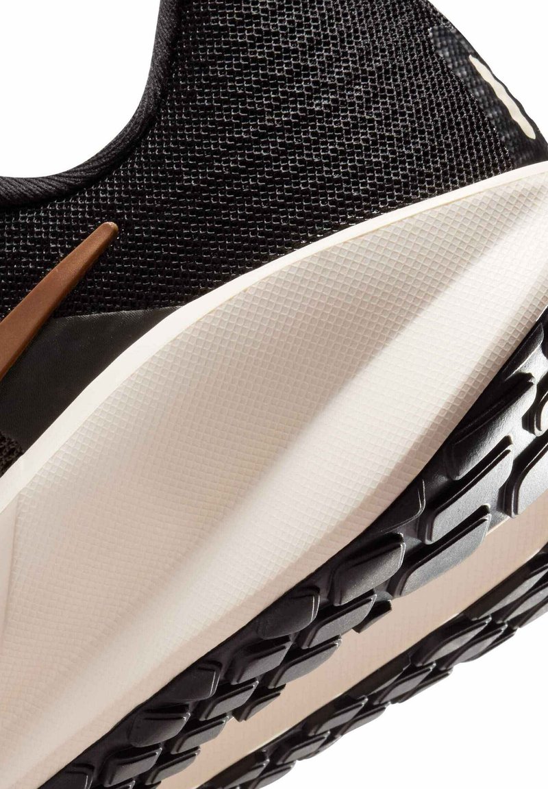 Zwarte sportschoen met een gestructureerde mesh bovenkant, bruine accenten en een dikke, crèmekleurige tussenzool. De buitenzool heeft een patroon voor extra grip.