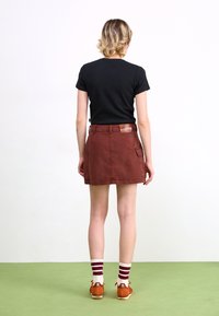 Camicia nera a maniche corte abbinata a una gonna color ruggine con tasche e dettagli a toppa. Calzature comprendono scarpe arancioni con calze a righe.