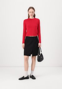 Top rosso a maniche lunghe, gonna nera a portafoglio con tasche laterali, calze grigie chiare, mocassini neri e una borsa a spalla nera. Stile semplice e moderno.