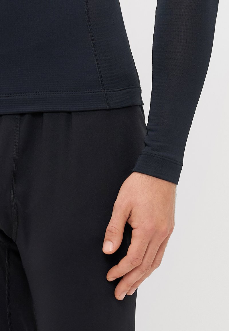 Zwarte lange mouwen sporttop gemaakt van een gladde, rekbare stof, met een naadloze zoom en aangesloten mouwen, gecombineerd met zwarte sportbroeken.