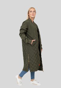 Pikowana, oliwkowa trench coat z wysokim kołnierzem, przednim zamkiem błyskawicznym i bocznymi kieszeniami. Długie rękawy i lekko luźny krój. Białe sneakersy.