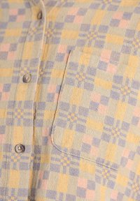 Chemise à manches courtes avec un motif à carreaux dans des couleurs jaune, bleue et rose. Comprend une poche poitrine et des boutons le long de la patte d'ouverture.