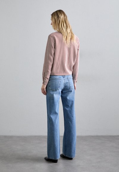 Κırσά μανίκια με κόκκινες και λευκές ρίγες, συνδυασμένο με ανοιχτό μπλε παντελόνι με φαρδιά πόδια. Το παντελόνι έχει κλασική γραμμή και δύο πίσω τσέπες.