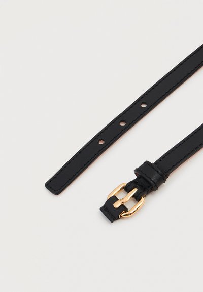 Λεπτή μαύρη δερμάτινη ζώνη με χρυσή μεταλλική αγκράφα και πολλαπλές τρύπες ρύθμισης, τοποθετημένη επίπεδα σε λευκό φόντο.