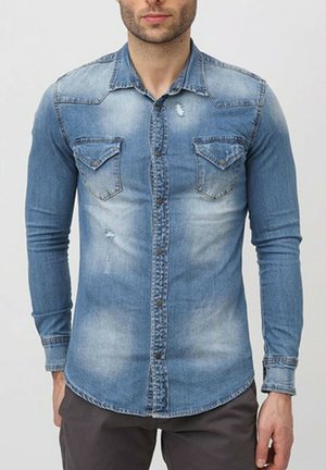 Chemise en jean à manches longues de couleur bleu clair avec un aspect délavé, fermeture par boutons à l'avant, et deux poches poitrine avec des rabats pointus.