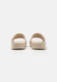 Sandale slip-on bej cu spate deschis, margini rotunjite și textură netedă, mată. Design simplu, fără hardware sau modele vizibile.
