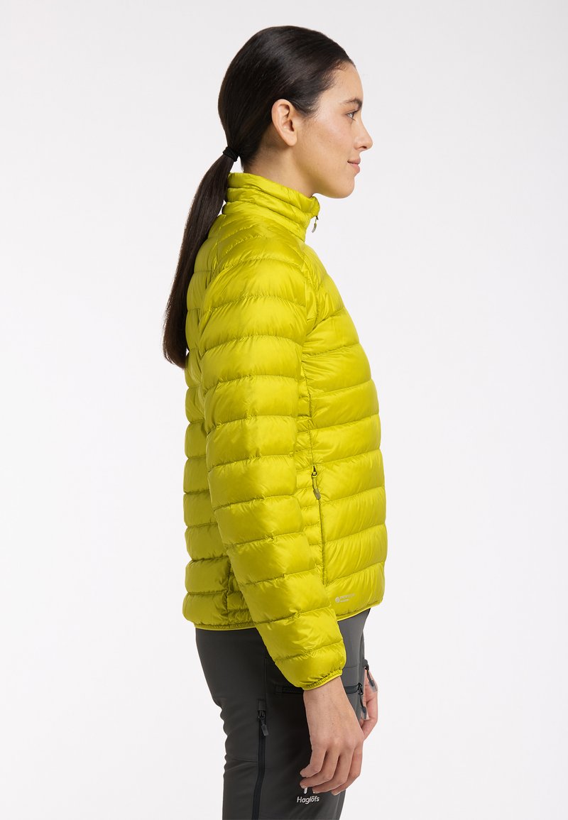 Limegrüne Daunenjacke mit hohem Kragen und horizontalen Nähten. Verfügt über seitliche Reißverschlusstaschen und elastische Bündchen für eine enge Passform.