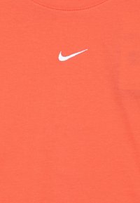 Tricou din bumbac coral portocalie cu guler rotund și logo-ul alb Nike swoosh pe față. Textură netedă, design minimalist.