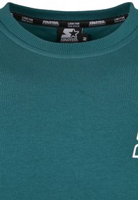 Col de sweat-shirt à col rond turquoise avec étiquette de la marque Starter et étiquettes noires à l'intérieur du col indiquant "CHERCHEZ L'ÉTOILE."