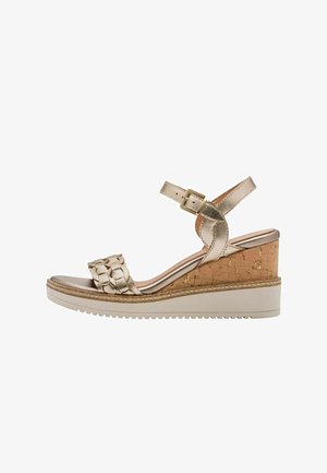 Wedge sandal in metallic gold with a woven strap, cork heel, and white rubber sole. Features a buckle for adjustable fit.