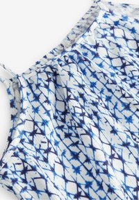 Niebieska i biała top bez rękawów w wzory, z cienkimi ramiączkami i teksturowanym materiałem, ukazującym geometryczny wzór.