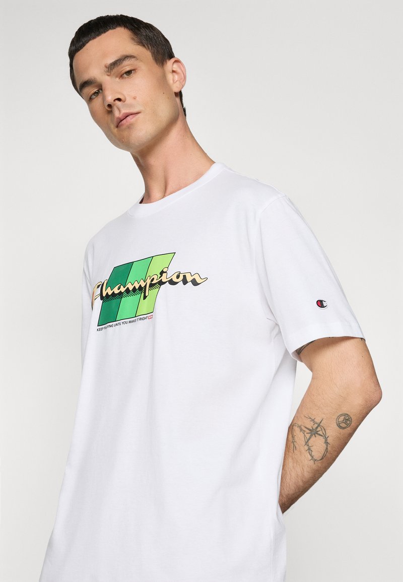 Camiseta de algodón blanca con un gráfico en verde y amarillo del logo "Champion", mangas cortas, cuello redondo estándar y logo bordado en la manga.
