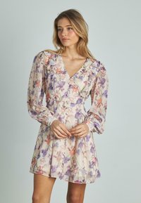 Vestido corto floral de tejido ligero con escote en V, hombros con volantes y mangas largas. Los colores incluyen púrpura, rosa y crema.