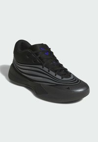 Chaussure de sport noire en matériau synthétique lisse, avec des rayures grises, un système de laçage et une semelle en caoutchouc texturée. Accents violets visibles.