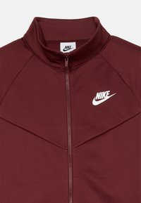 Μπορντό φούτερ ζακέτα με λείο ύφασμα, διαθέτει ψηλό γιακά και λογότυπο Nike σε λευκό χρώμα στην επάνω αριστερή πλευρά.