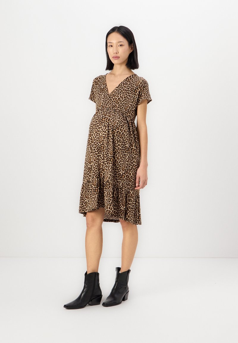 Leopard print dress with a v-neckline, short sleeves, and a tiered skirt. Worn with black ankle boots, showcasing a casual, flowing design.