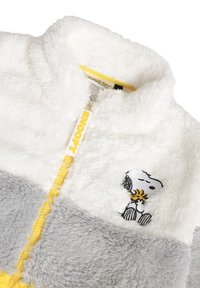 Chaqueta de felpa sintética con cierre en blanco y gris, con una cremallera amarilla y una etiqueta de "Snoopy", y un diseño bordado de Snoopy en el pecho.