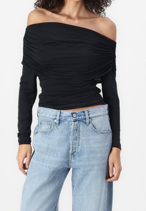 Haut noir à épaule dénudée avec texture froncée au niveau du corsage, manches longues, associé à un jean taille haute bleu clair avec poches latérales et un bouton.