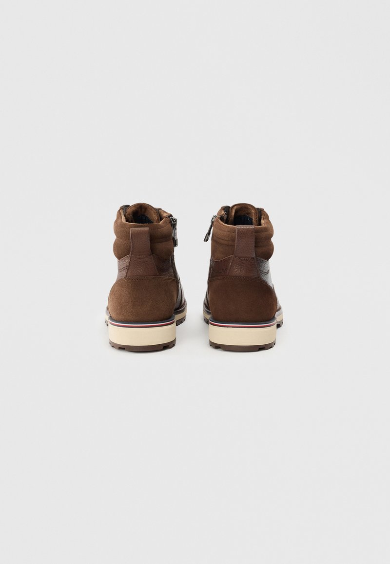 Bottines en suede marron avec des accents en cuir lisse, un col rembourré, une fermeture éclair à l'arrière et une semelle en caoutchouc beige et foncé.