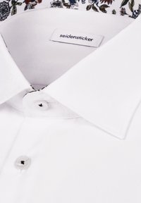 Chemise blanche à col pointu, doublure intérieure fleurie et étiquette de marque "seidensticker" cousue à l'intérieur du col.