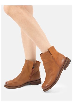 Enkellaarsjes van bruin leer met ritssluitingen aan de zijkant, gedragen op gekruiste benen tegen een witte achtergrond.