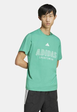 Camiseta de algodón verde con cuello redondo, que presenta el texto y el logo en blanco "ADIDAS SPORTSWEAR". Combinada con pantalones cortos negros con estampado.