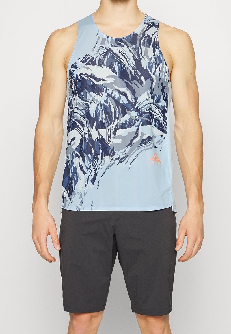 Top deportivo de color azul claro con un patrón abstracto en navy y blanco, con una etiqueta en la parte inferior derecha y un cuello redondo. Combinado con pantalones cortos negros.