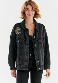 Czarna dżinsowa kurtka o luźnym kroju, z dwoma przednimi kieszeniami, zatrzaskami i haftowanym, vintage napisem na piersi.