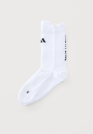 Par de calcetines blancos tobilleros con un logo negro cerca de la parte superior y una pequeña letra negra "R" en la punta.