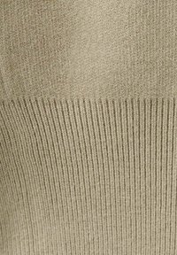 Naadloze gebreide trui in een gedempte beige tint. Heeft een geribbelde textuur aan de zoom met een glad bovenste gedeelte, wat een duidelijk contrast creëert.