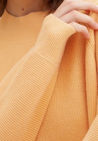 Sweter z prążkowanego dzianiny w miękkim, brzoskwiniowym kolorze, z wysokim kołnierzem i dopasowanymi rękawami, prezentujący ciepłą teksturę i wygodny fason.