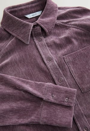 Langärmliges Hemd aus schimmerndem lila Stoff. Mit einer durchgehenden Knopfleiste, Kragen und einer einzelnen Brusttasche. Weiches, strukturiertes Material.
