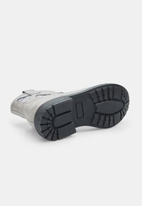 Zapato de ante gris con una suela de goma negra, que cuenta con un patrón de textura en la suela y una correa de velcro para un ajuste seguro.