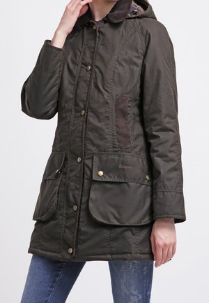 Olivekowy pikowany płaszcz z kapturem, z wieloma przednimi kieszeniami, brązowymi akcentami i zapięciem na zatrzaski. Teksturowany materiał z klasycznym wzornictwem.
