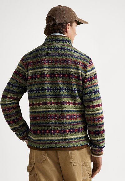 Vilnos striukė su įvairiaspalviais geometriniais raštais ant žalsvo fono, aukštu apykakliu ir tekstūriniu paviršiumi. Rudi akcentai apačioje.