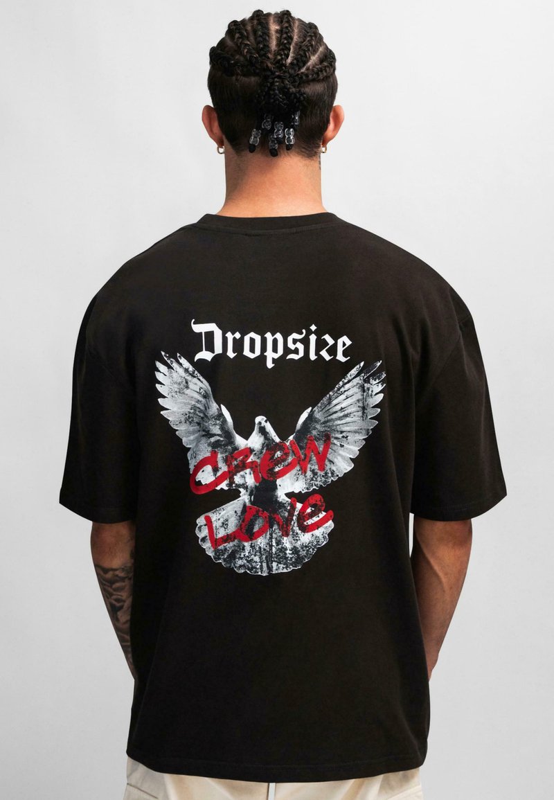 Zwarte katoenen t-shirt met een oversized pasvorm, met een grote witte adelaar graphic en rode tekst "CREW LOVE" op de achterkant.