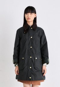 Dark green waterproof coat with a brown collar, gold snap buttons, two front pockets, and plaid accents on sleeves.