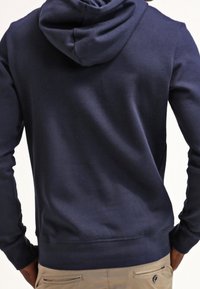 Sudadera con capucha azul marino de tela de algodón, con capucha ajustable mediante cordón, puños acanalados y dobladillo plano sin gráficos ni adornos visibles.