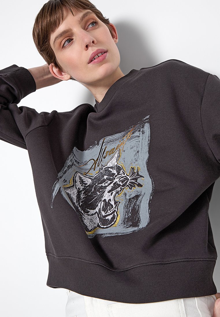 Schwarzer Sweatshirt mit Rundhalsausschnitt und verkürzt geschnittener Form, der ein grafisches Druckmotiv eines brüllenden Tieres in Grau und goldenen Akzenten zeigt.