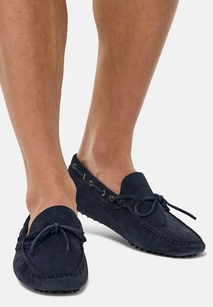 Marineblaue Wildlederschuhe mit runder Zehenform, Schnürverschluss und goldfarbenen Ösen. Texturiertes Profil mit kleinen Vorsprüngen für besseren Grip.